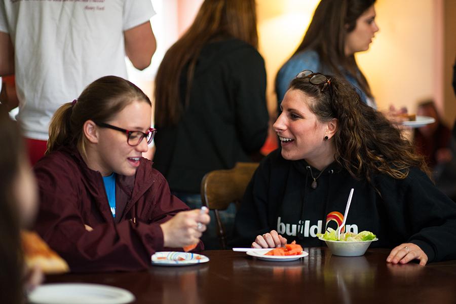 Two students sit together eating fruit and salad.