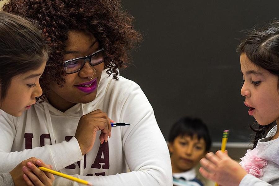 An education student with a nose ring helps two young girls with their school assignment.