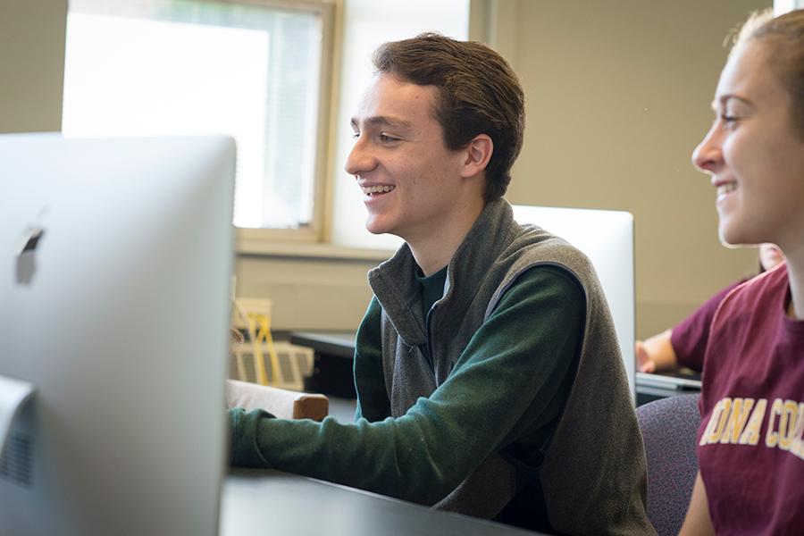 Two students smile and work at an iMac in the computer lab.