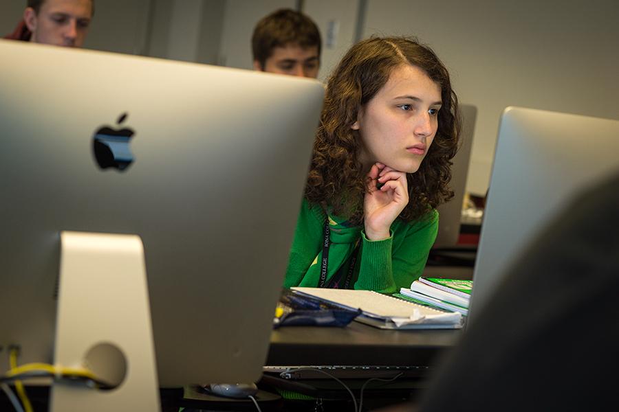 A student sits between two iMacs and works in the computer lab.