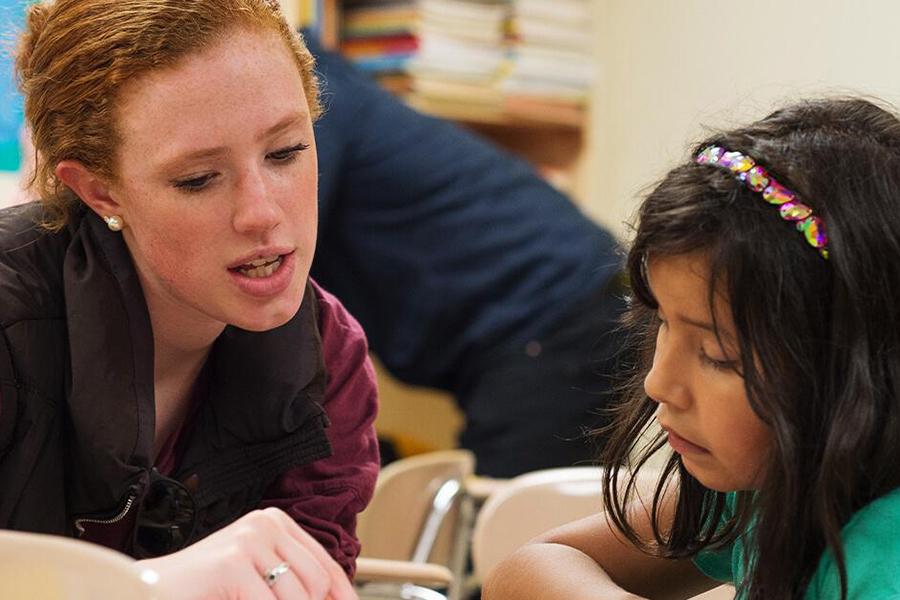 A speech communication major helps a young girl sound something out in a classroom.
