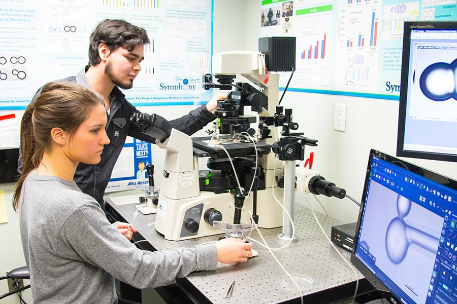 A male student and female student use chemistry equipment while looking over a computer monitor