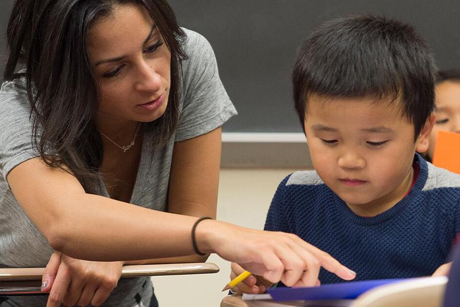 An education student helps a young boy with his assignment by pointing out something.