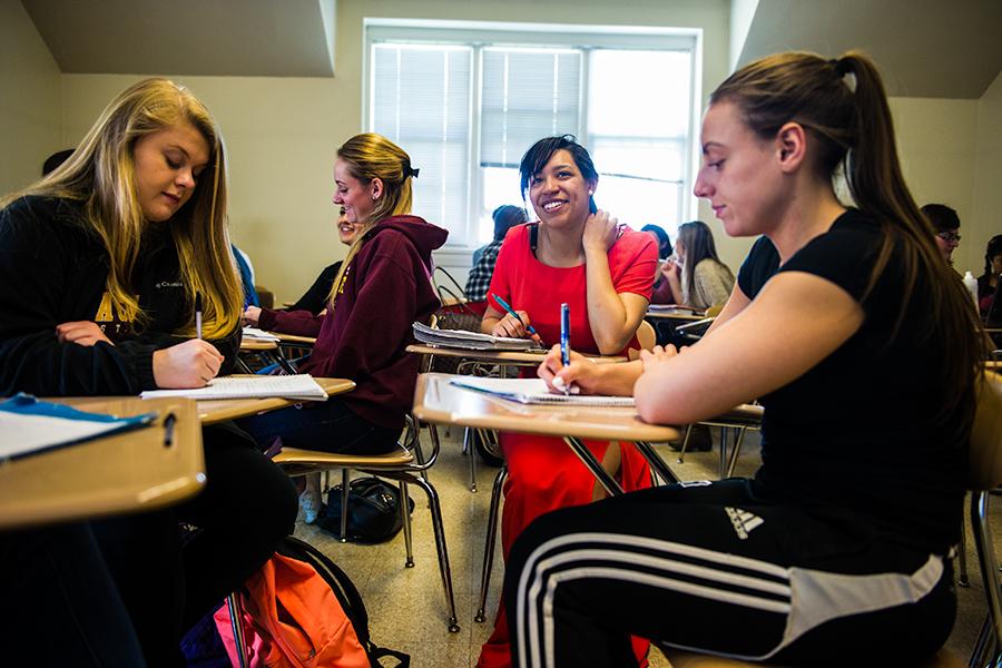 Four female students sit at desks in a classroom writing notes for their psychology class.