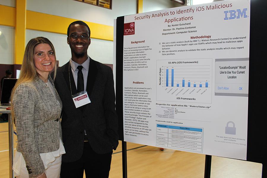A student and his computer science professor stand near his poster at Iona Scholars Day.