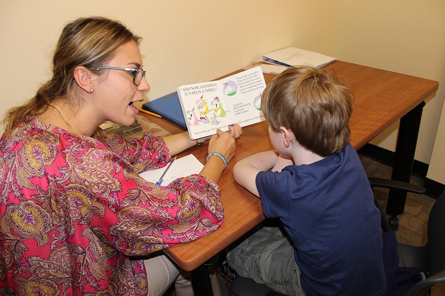 A speech communicatin major reads a young boy a book and helps him sound something out.