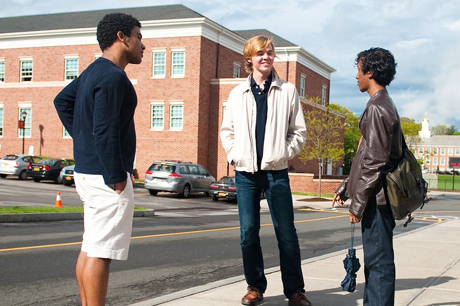 Three students stand on the sidewalk outside of Spellman and talk.