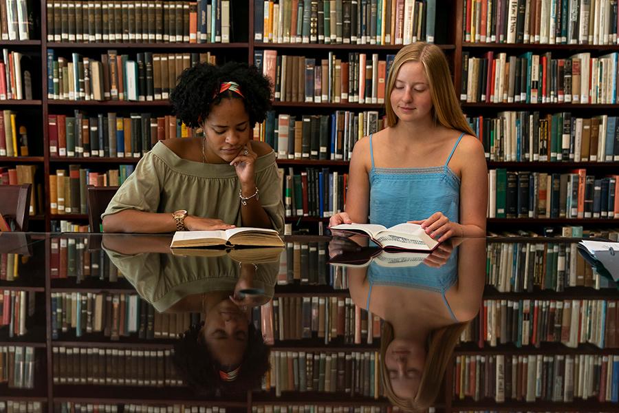 Two students sit in the library to read books for a history class.