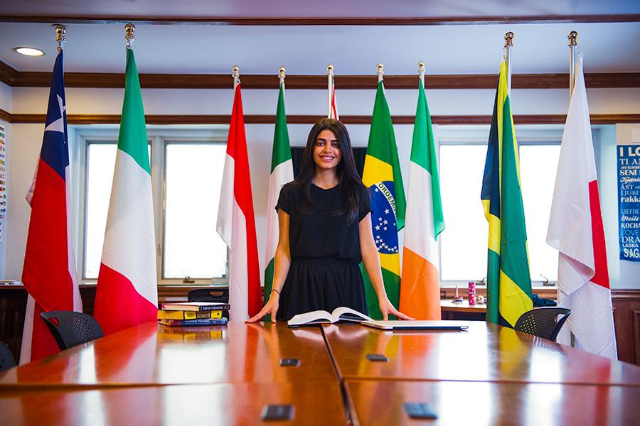 An international business student stands in front of a row of flags from several different countries.