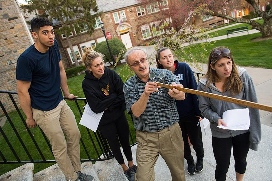 A group of students gather around a professor for a physics class.