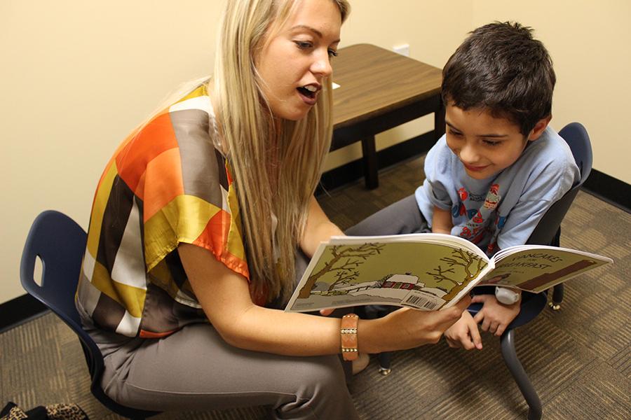A speech therapist reads a book to a young client.