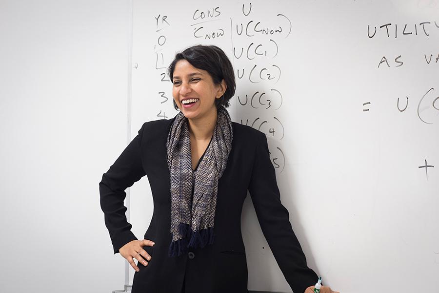 A professor stands in front of the white board and smiles.