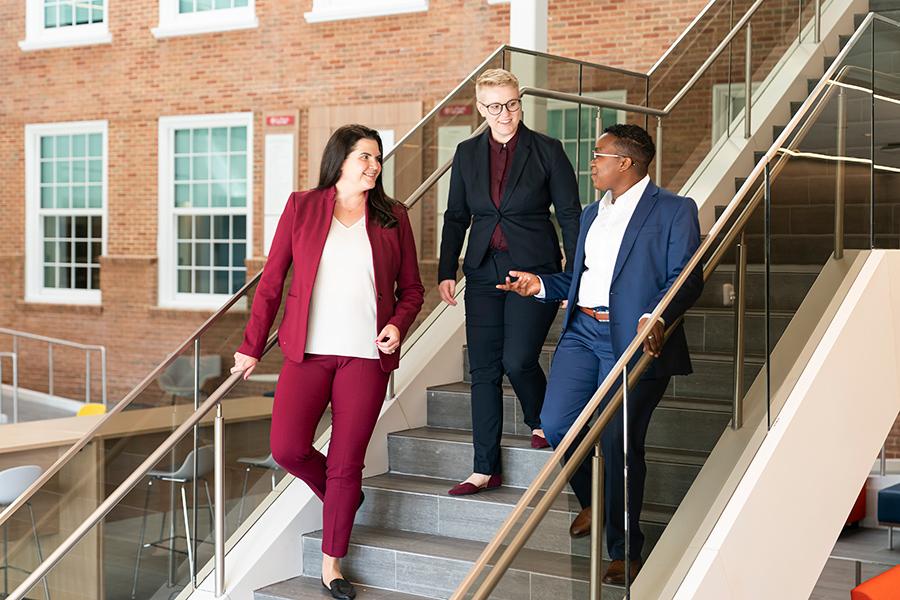 Three graduate students walk down the stairs in the LaPenta School of Business.