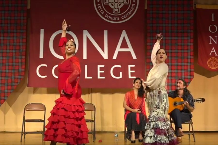 Two flamenco dancers end their dance with one arm in the air. There is a guitar player and another dancer in the background sitting on chairs.