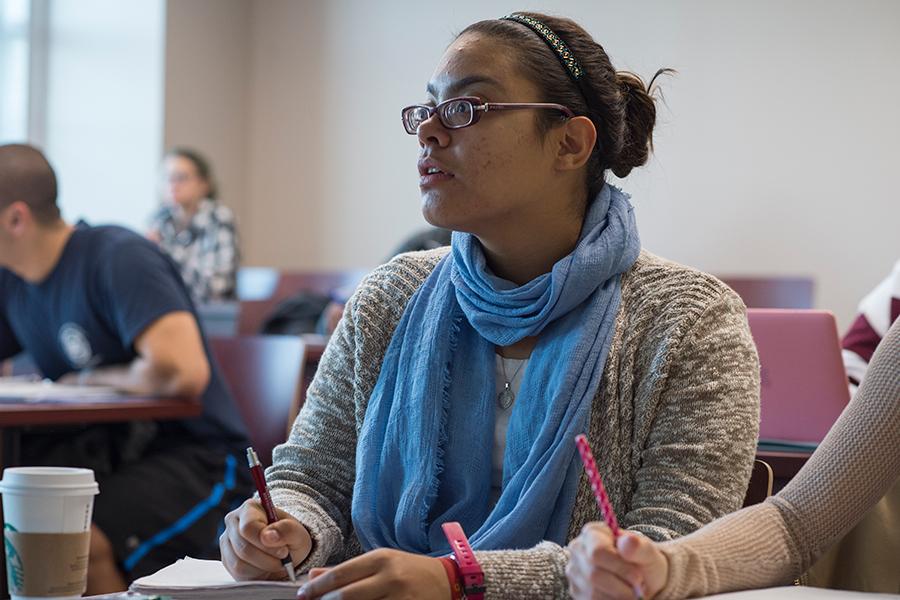 An attentive student looks up towards the professor while writing something down.