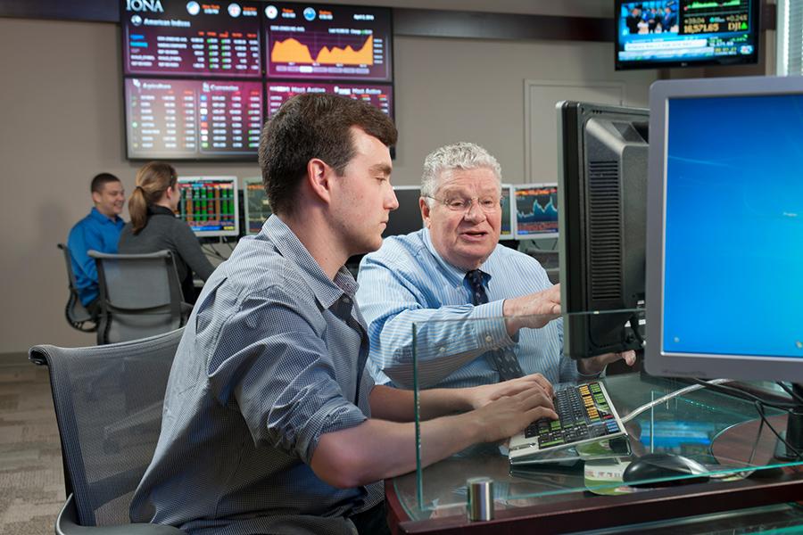 A finance professor assits a student on a Bloomberg station in the trading floor lab.