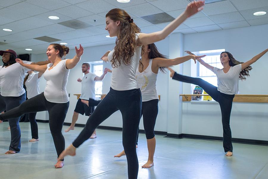 Students in a dance class lift their arms and their right legs in the air.