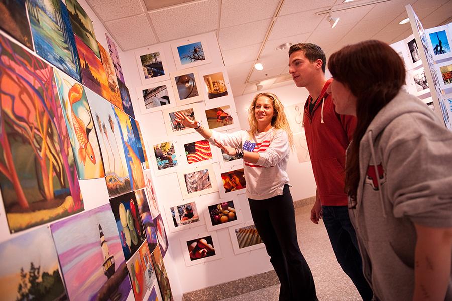 Three students stand in the art gallery while one students explains a painting.