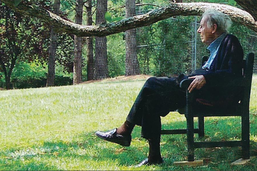 Thomas Berry sitting on a bench beside a tree.