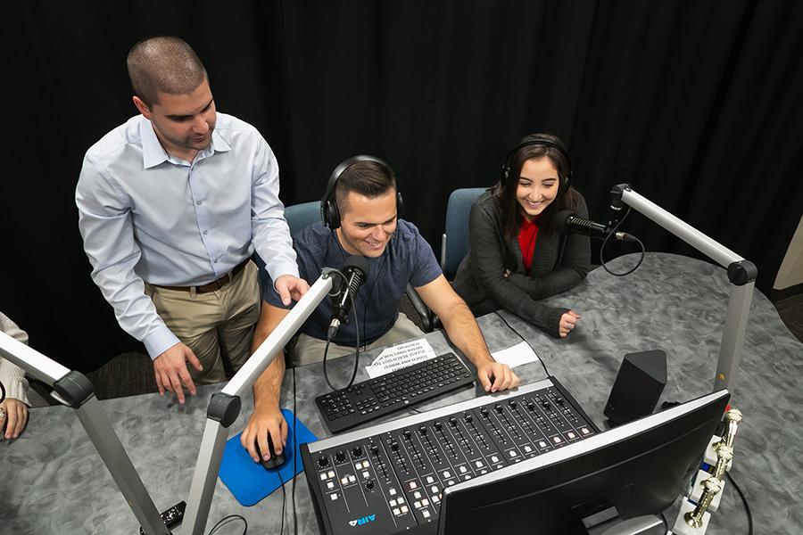 Joe from Media & Strategic Communication department shows three students how to use the mixing board.