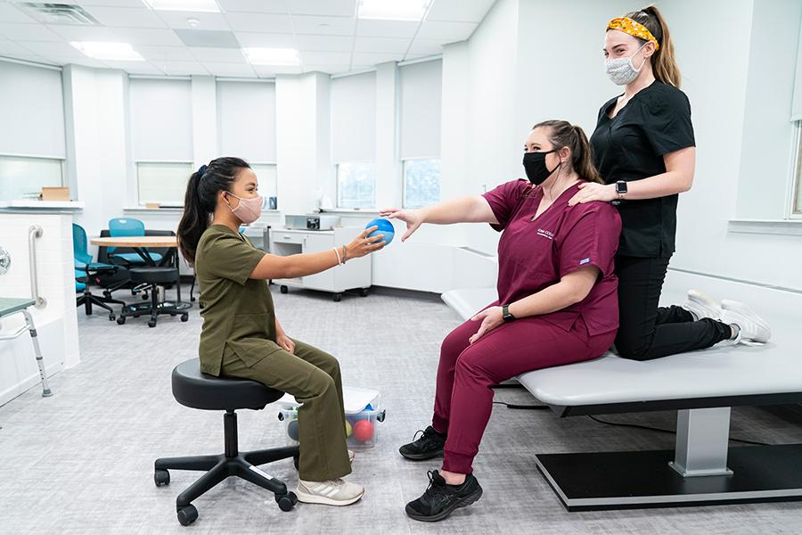 Three occupational therapy students practice handing a ball back and forth as one of their grip exercises.