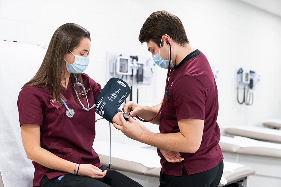 Two nursing students practice measuring someone's blood pressure.