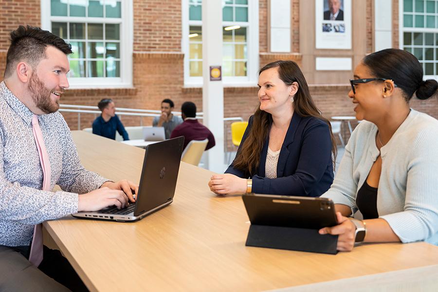 Three students work on laptops in the atrium in LaPenta School of Business.