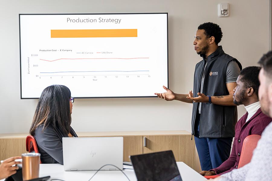 Students work in a conference room in the LePenta School of Business and their Production Strategy is projected on a screen.