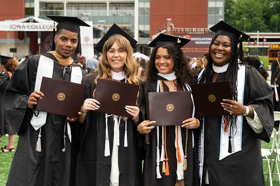 Four graduates hold their degrees and smile at the 2021 in-person recognition ceremony.