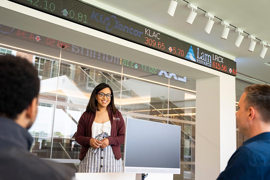 A student stands in front of the ticker and does a presentation in the LaPenta School of Business trading floor.