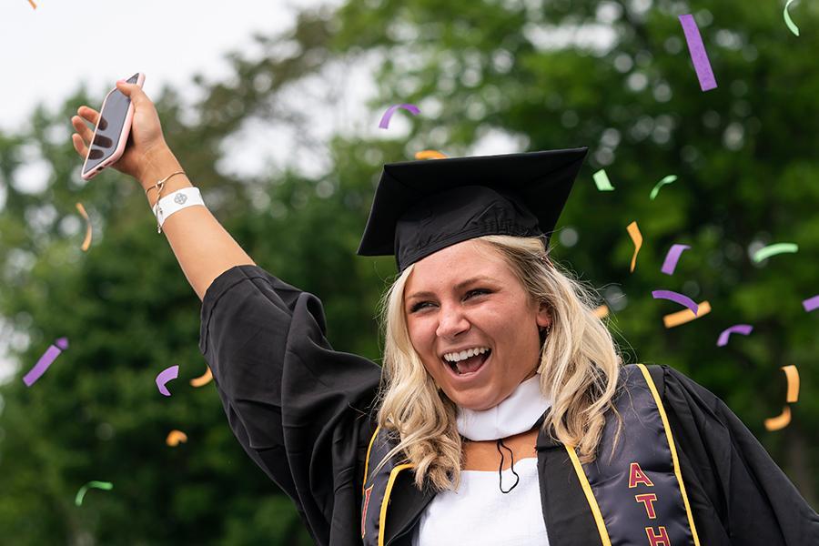 A student raises her hand in celebration while confetti comes down behind her.