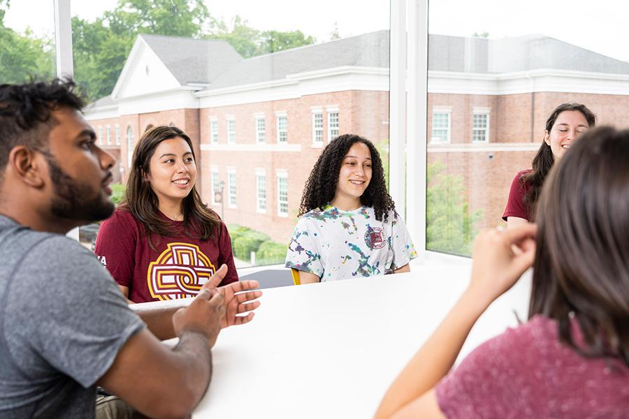 Students sit and talk around a table at the Hynes Institute.