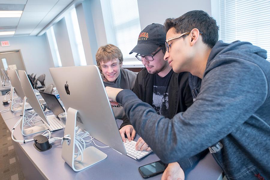 Three students work together at a computer for their minor in business analytics.