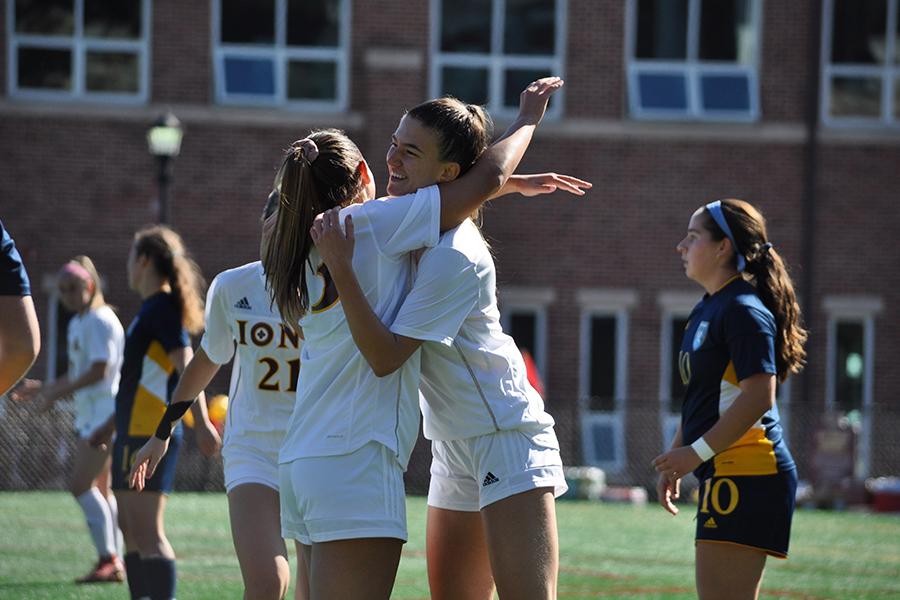 Two players hug and smile after a goal during a women's club soccer game.