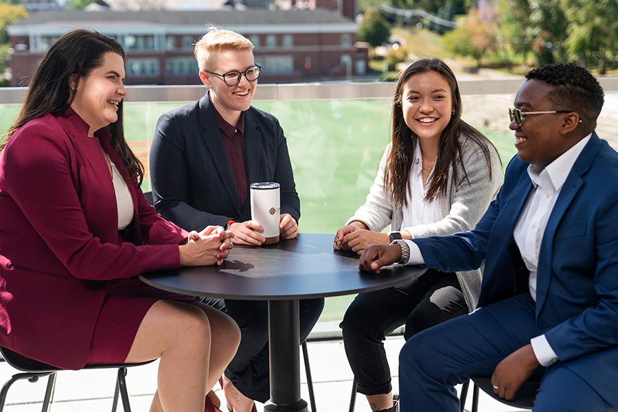 Four LSB grad students sit outside and chat with caption.