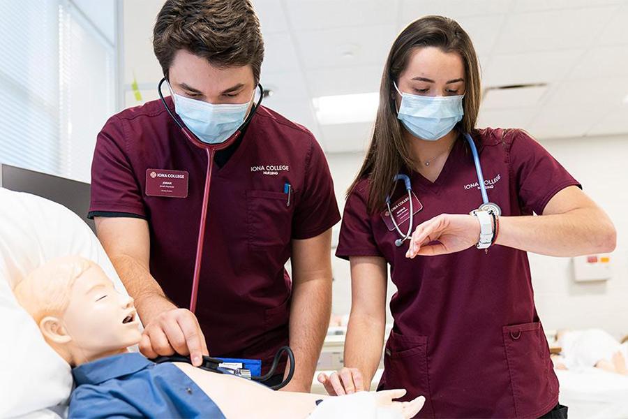 Two Iona nursing students practice skills on a human mannequin with caption.