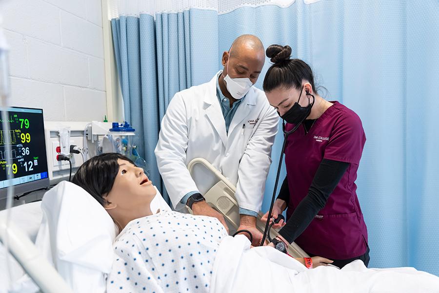 A nursing student takes the blood pressure on a mannequin patient.