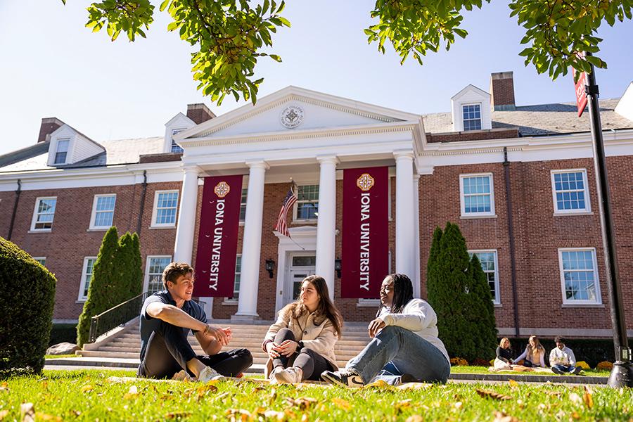 Three students sit outside of McSpedon Hall on a sunny day.