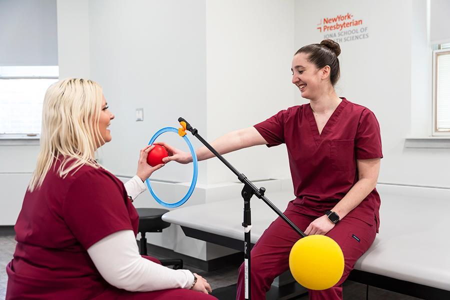 Two OT students practice movements with a red ball.