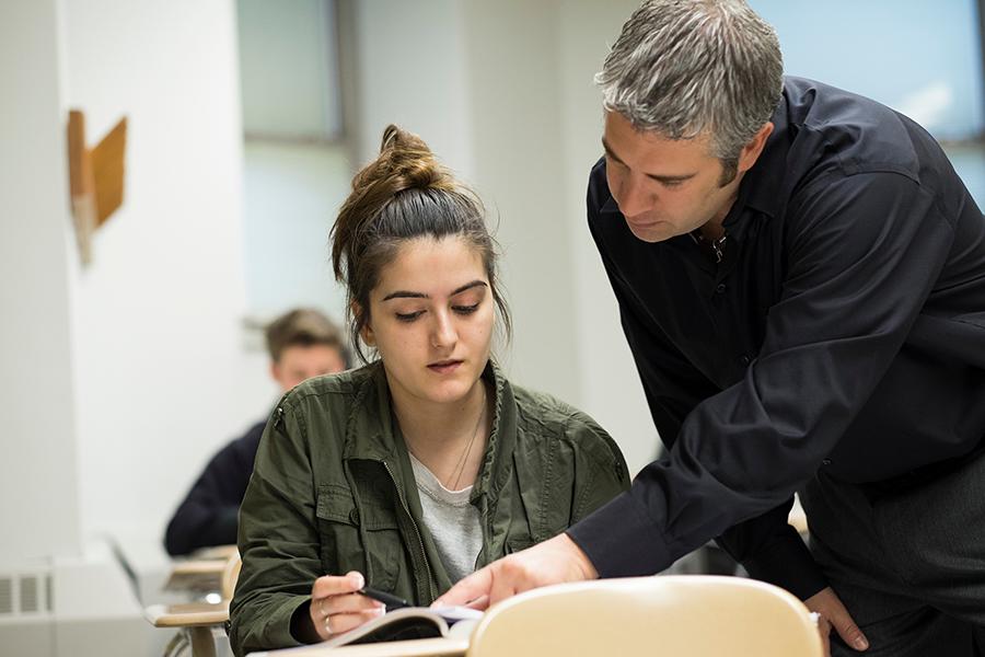 A professor helps a student with a problem in a textbook.