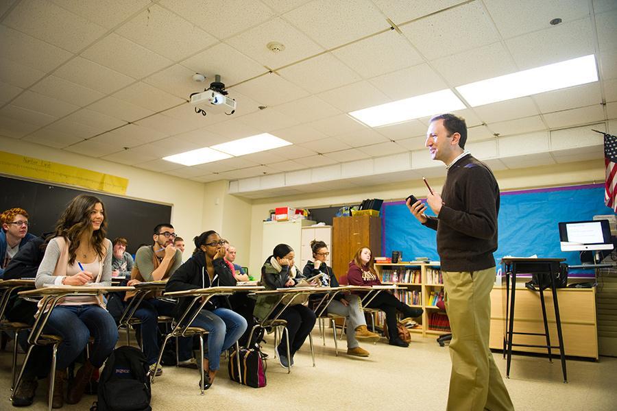 A teacher in the front of the classroom with an American flag in the background.