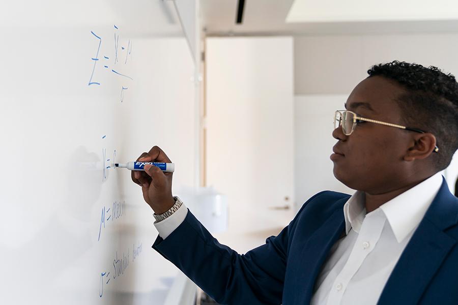 An MBA student works on equations on a white board.