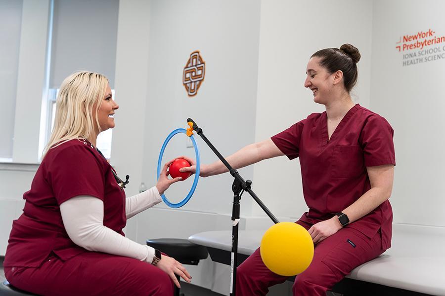 Two OT students practice movements with a red ball.