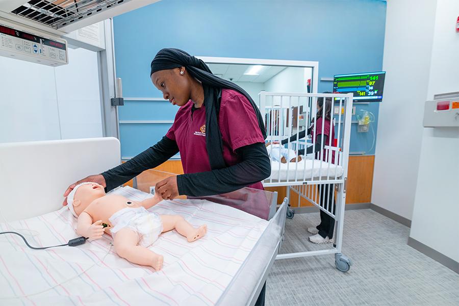 A nursing student works with an infant mannequin.