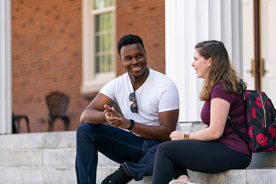 Two criminal justice students sit on the steps outside and talk.