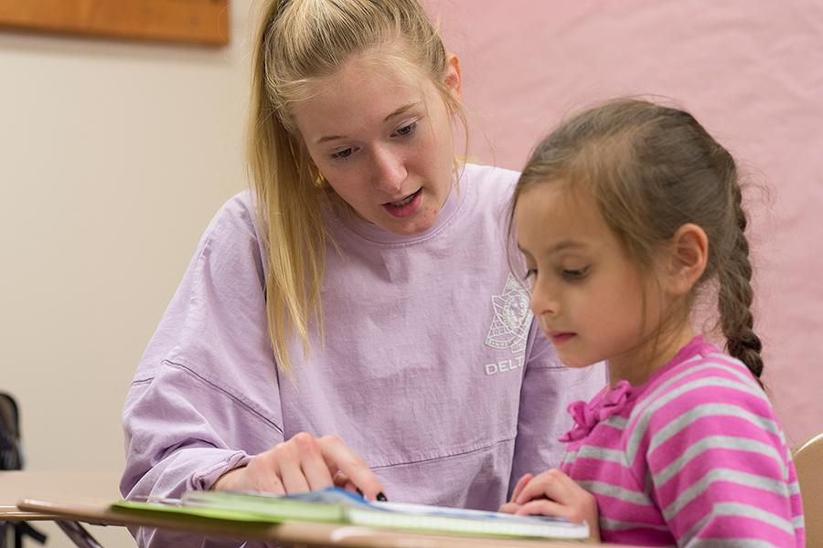 A literacy specialist in a pink sweater works with a student on reading.