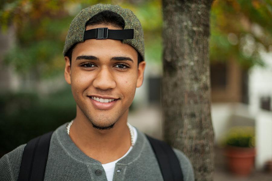 A student with a baseball cap smiles at the camera.