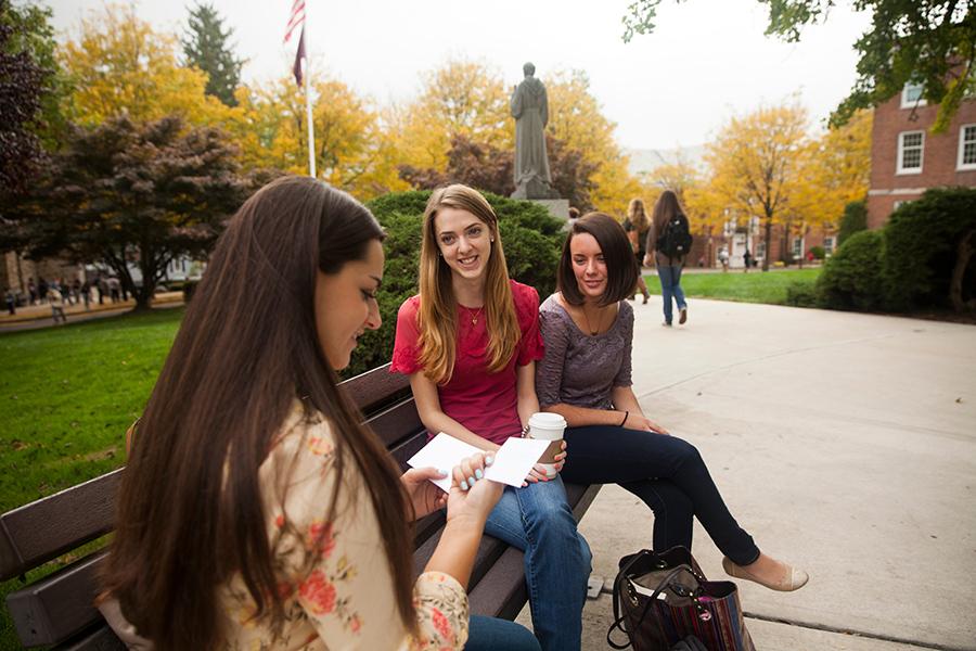 Three students sit on bench and study from flashcards.