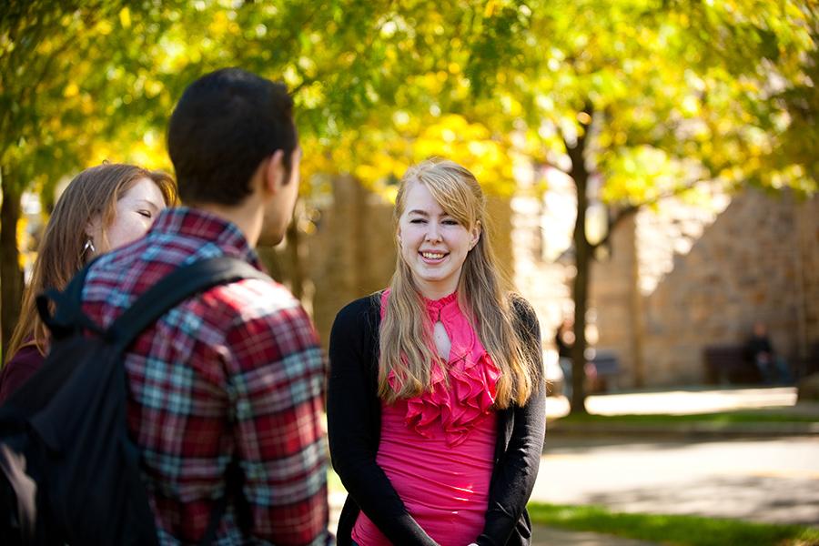 Three students stand and talk near the quad.