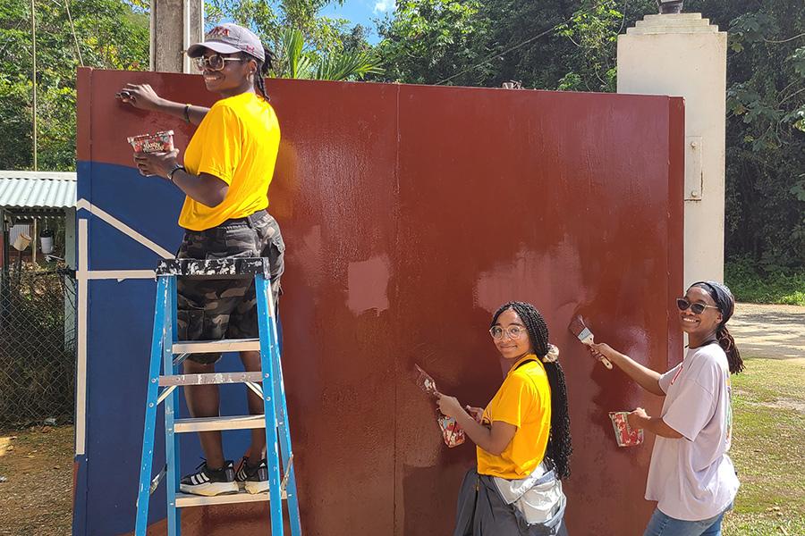 Students help to paint a building red during the service trip to Jamaica.